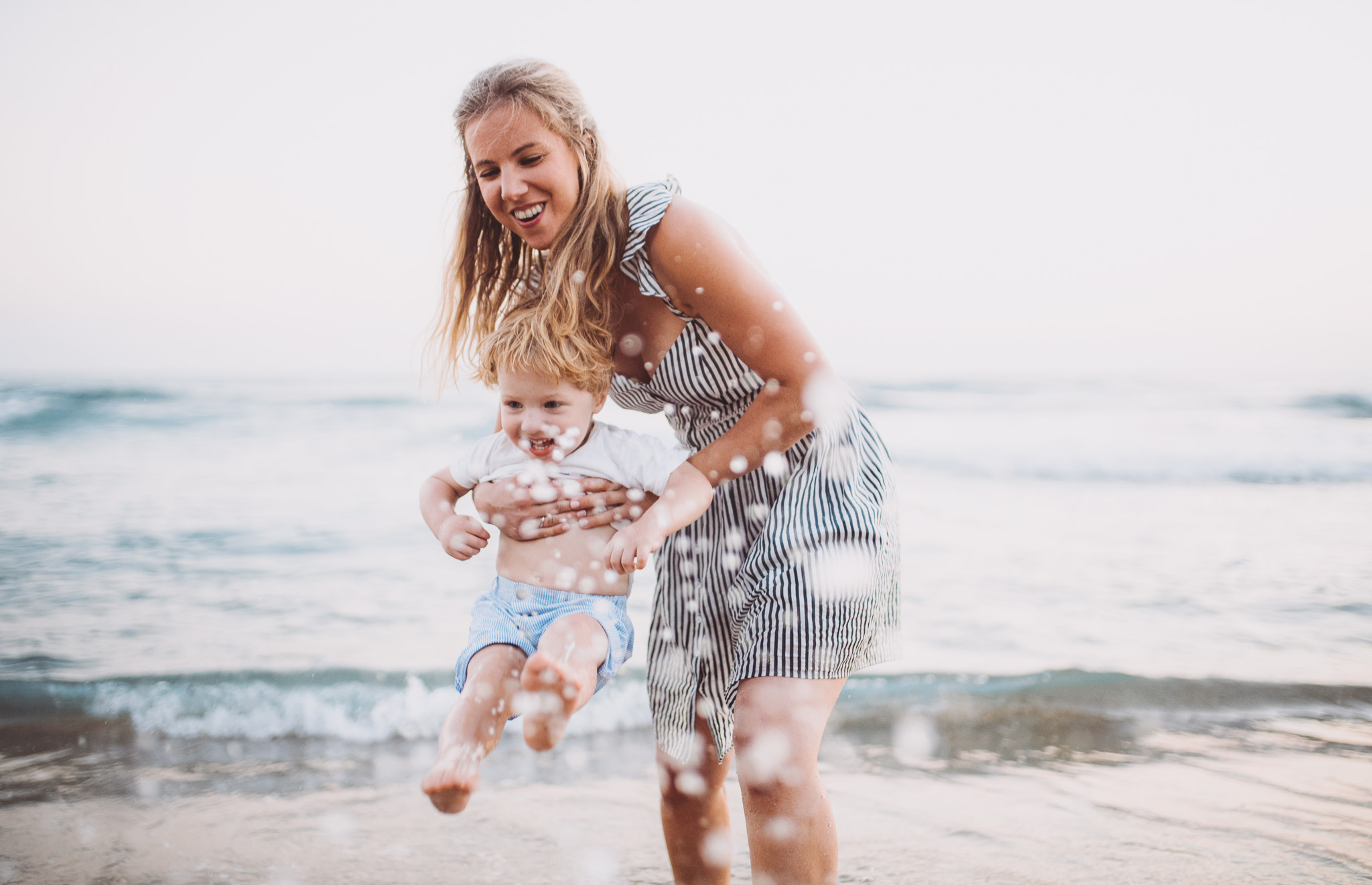 Junge Mutter tobt mit ihrem Kleinkind im flachen Wasser am Strand