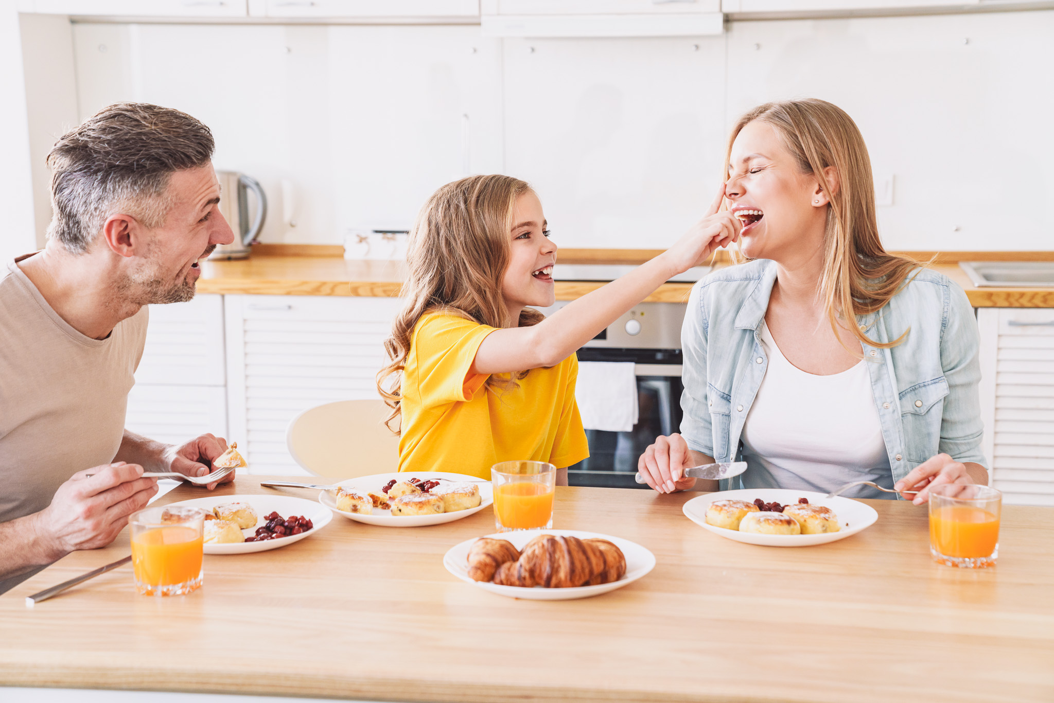 Familie sitzt beim Frühstück mit Croissants und Orangensaft